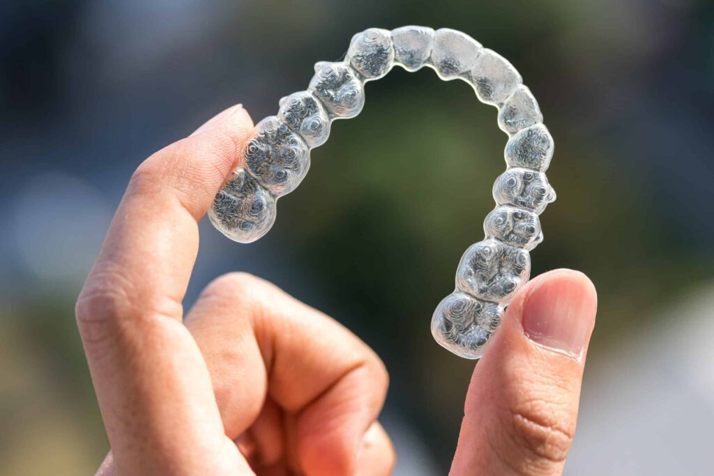 A hand holding a clear dental aligner with a blurred background, showcasing the hassle-free dentist experience for achieving a straighter smile.