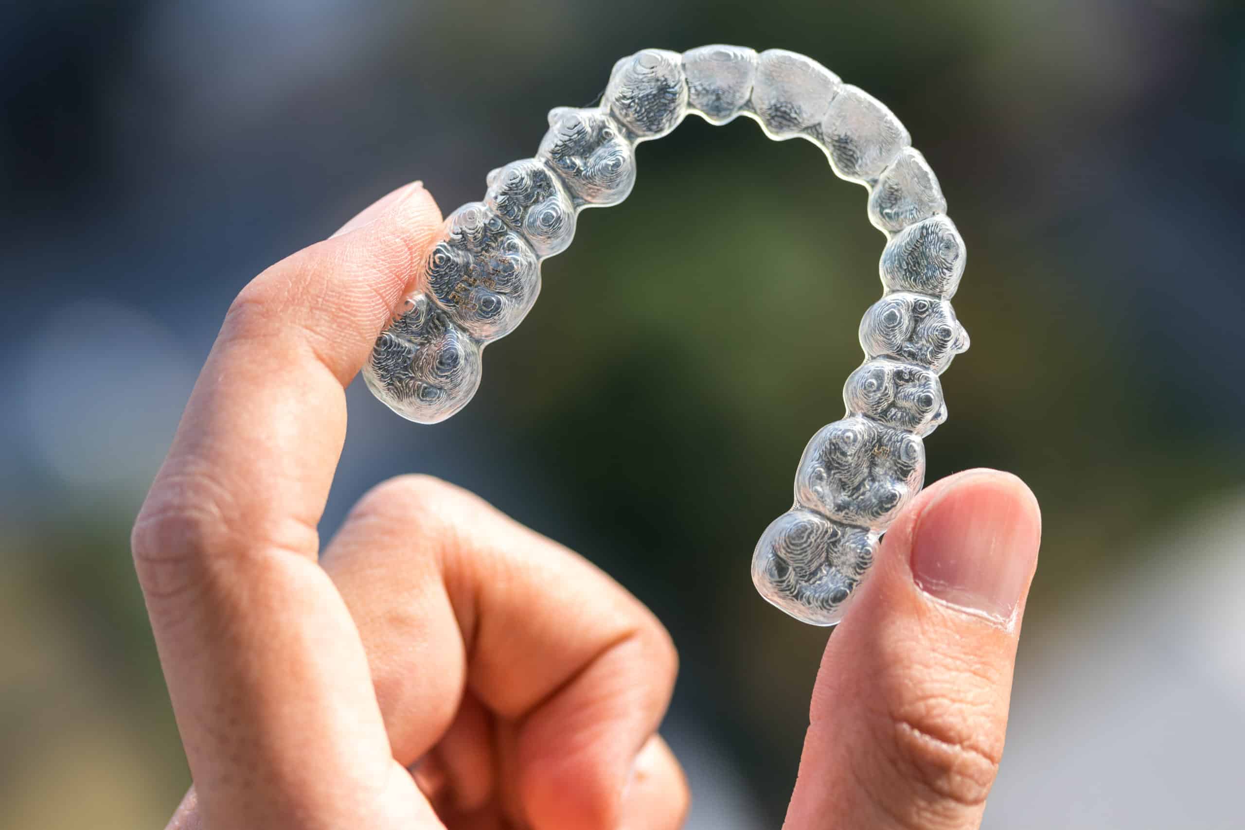 A hand holding a clear dental aligner with a blurred background, showcasing the hassle-free dentist experience for achieving a straighter smile.