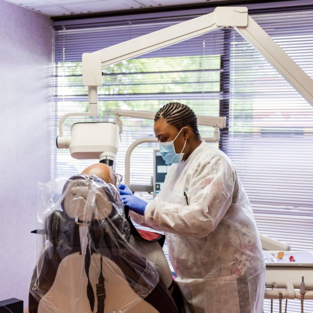 A dental professional wearing protective gear examines a patient in a dental clinic equipped with standard dental tools and equipment.