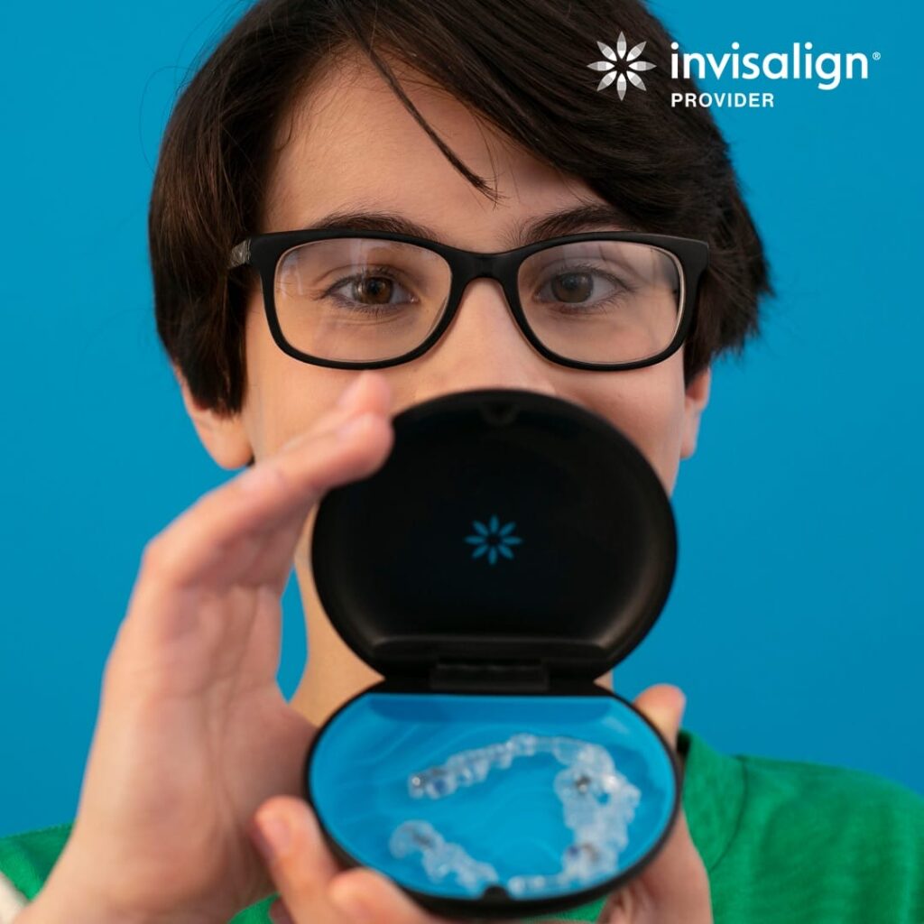Person holding an open Invisalign case with clear aligners inside, standing against a blue background, with "Invisalign Provider" logo in the top right corner.
