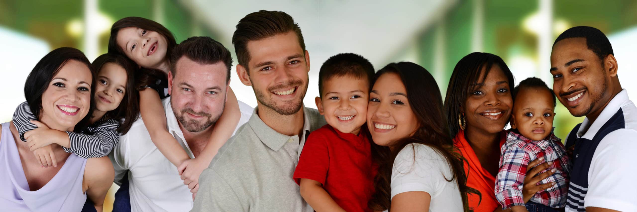 A group of diverse families, including adults and children, stand close together smiling in front of a blurred green and white background, their bright smiles reflecting the care of an affordable full service dentist.
