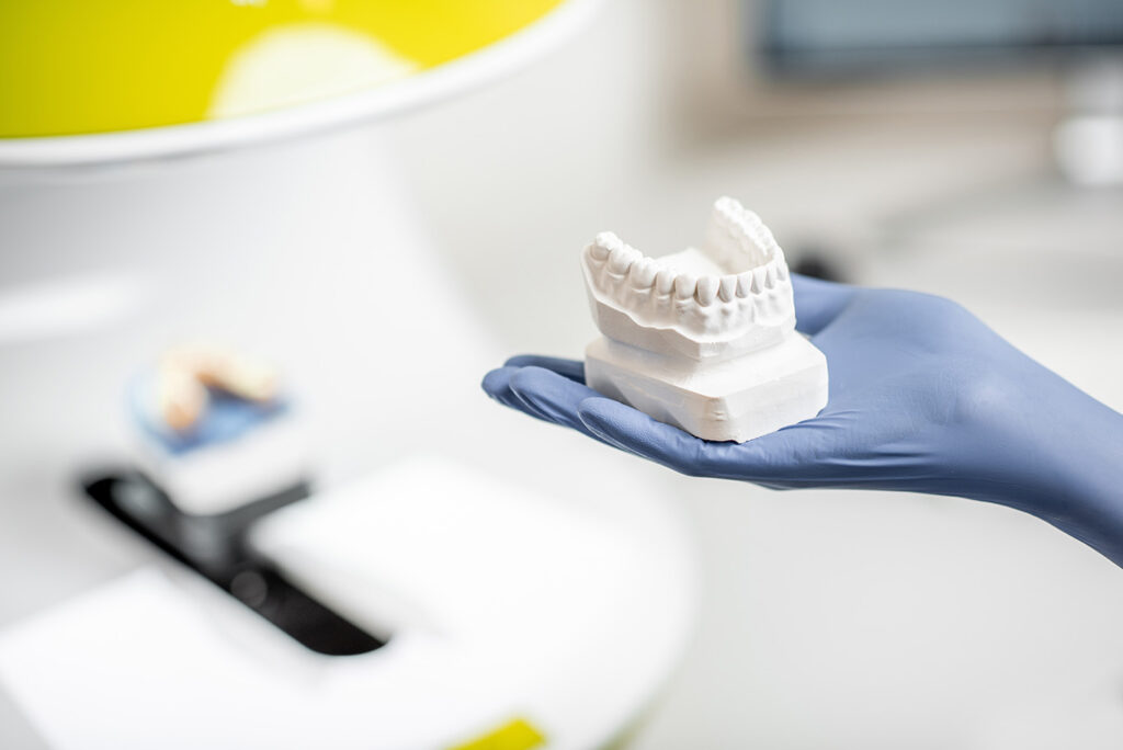 A gloved hand holds a white dental model of teeth, highlighting the importance of oral health, with dental diagnostic services equipment visible in the background.