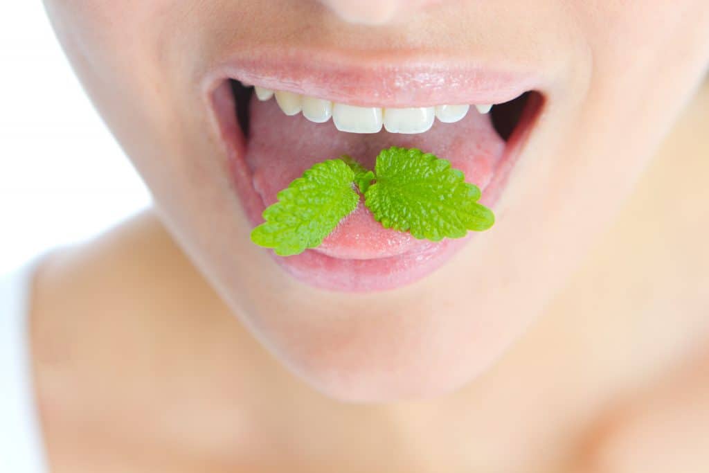 Close-up of a person’s open mouth with two green mint leaves resting on their tongue.