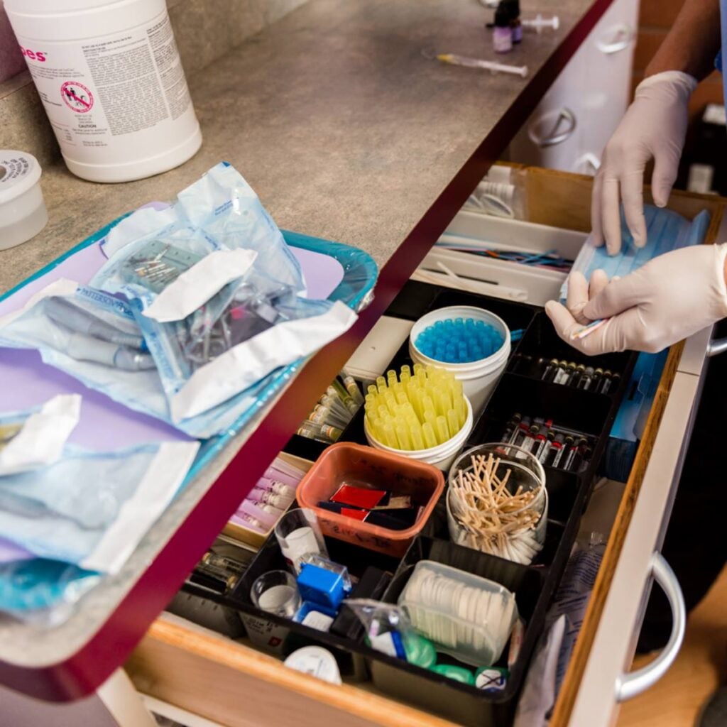 A person wearing gloves organizes orthodontics tools in a drawer, with various sterilized instruments and supplies for dental services visible on the counter and in the drawer.