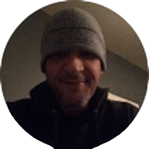 A person wearing a knit beanie and dark clothing smiles at the camera in a dimly lit room, reminiscent of the joyful moments often shared in the smile doctor reviews.