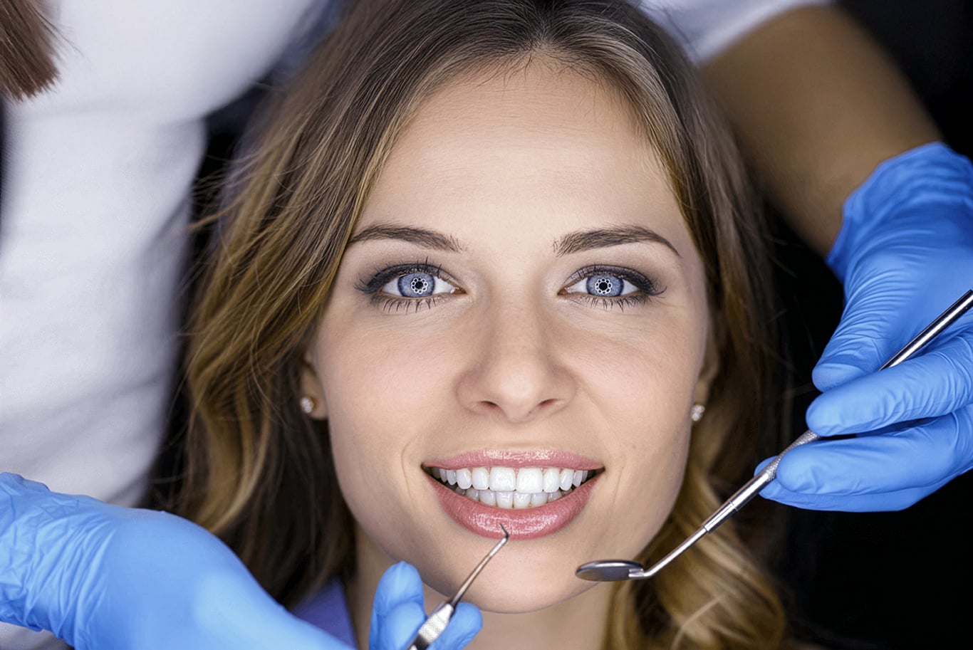 A woman with blue eyes smiles while a dentist, wearing blue gloves, examines her teeth using dental tools.